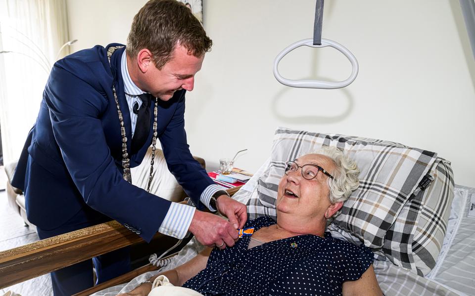 Eerbetoon aan het ziekbed. Raadslid Janny Mones-Kassies krijgt een koninklijke onderscheiding opgespeld door burgemeester Jouke Spoelstra.