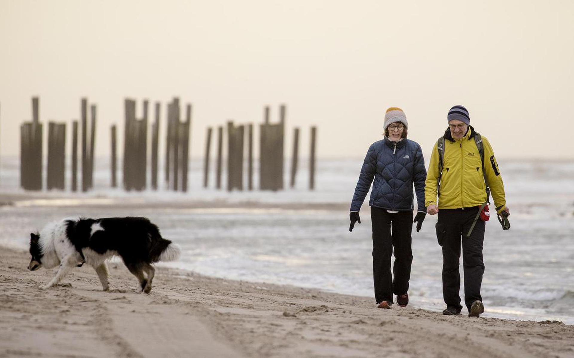 Wandelaars met een hond op het strand bij Petten. De eerste helft van de winter is zacht verlopen.