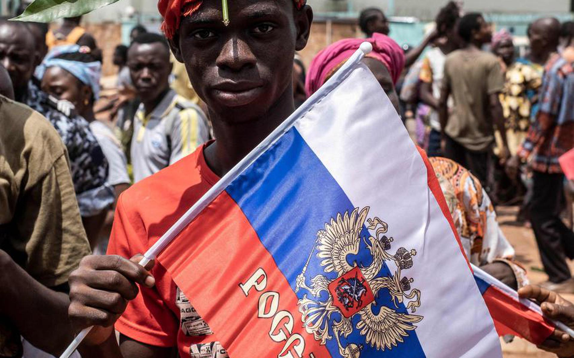 A demonstrator with foliage on to his head, a sign of compassion in Central African Republic, holds a Russian flag with the emblem of Russia on while posing for a portrait in Bangui, on March 22, 2023 during a march in support of Russia and China's presence in the Central African Republic. - Central African RepublicÂ authorities have opened an investigation into the deaths of nine Chinese nationals killed in an attack on a gold mine in the centre of the country on March 19, 2023. Taking advantage of the vacuum created by the departure of the bulk of French troops, Moscow sent "military instructors" to the country in 2018, then hundreds of Wagner paramilitaries in 2020 at the request of Bangui, faced with a threatening rebellion. (Photo by Barbara DEBOUT / AFP)