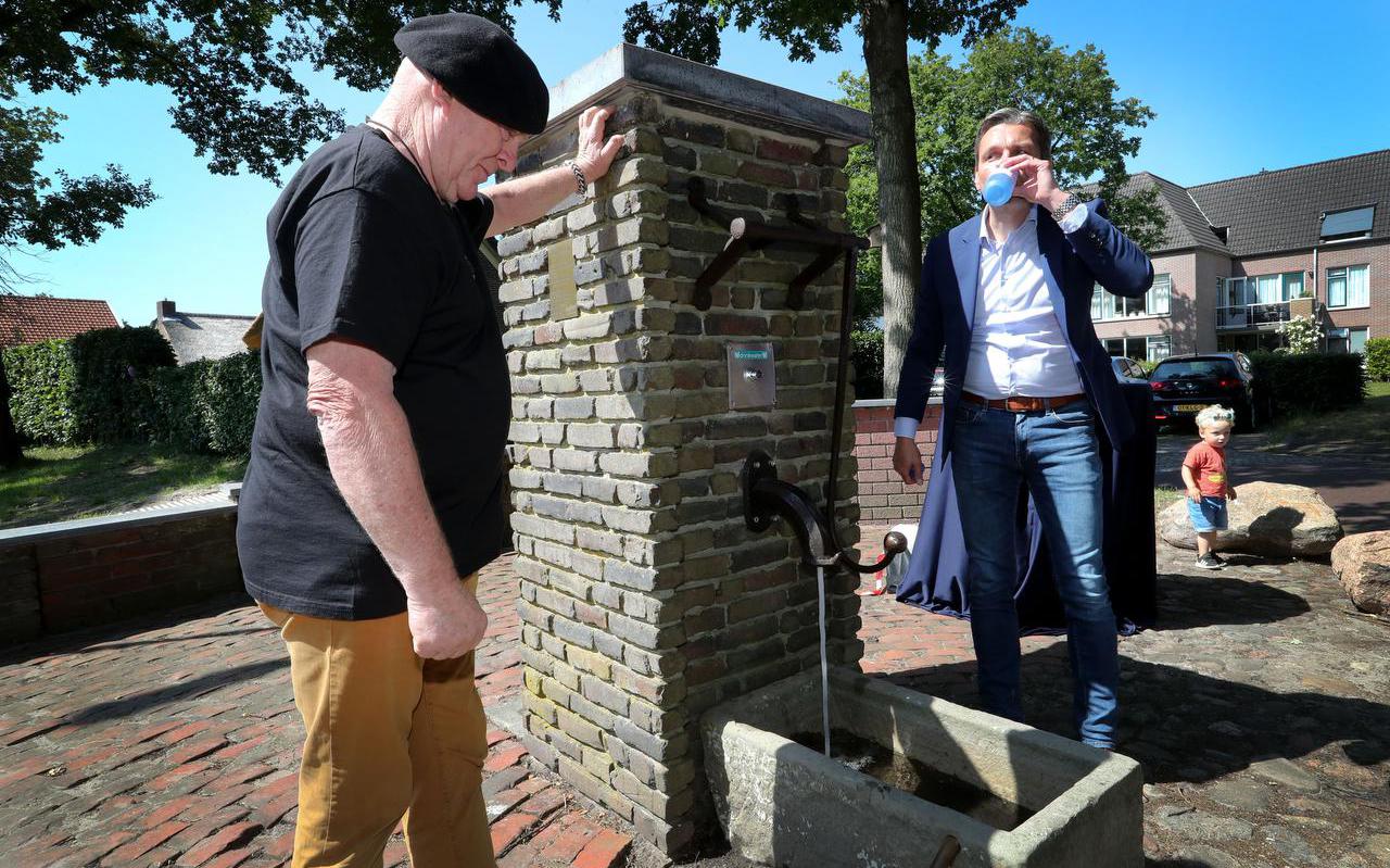Terwijl kunstenaar Arie Fonk (links ) de in oude luister herstelde pomp inspecteert, laat wethouder Ivo Berghuis zich de eerste slokken vers water smaken.          