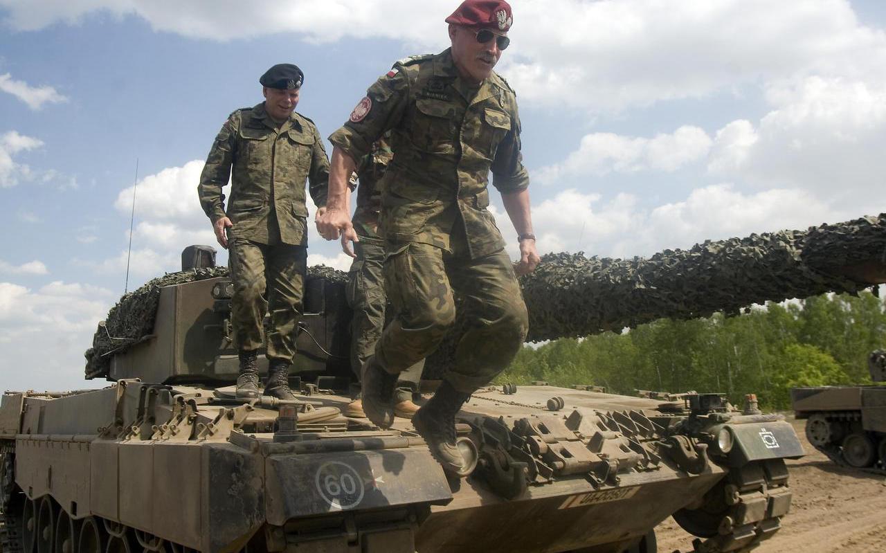 Generaal Bieniek, met rode paratroeper-baret, springt van een Leopard-tank tijdens een militaire oefening.