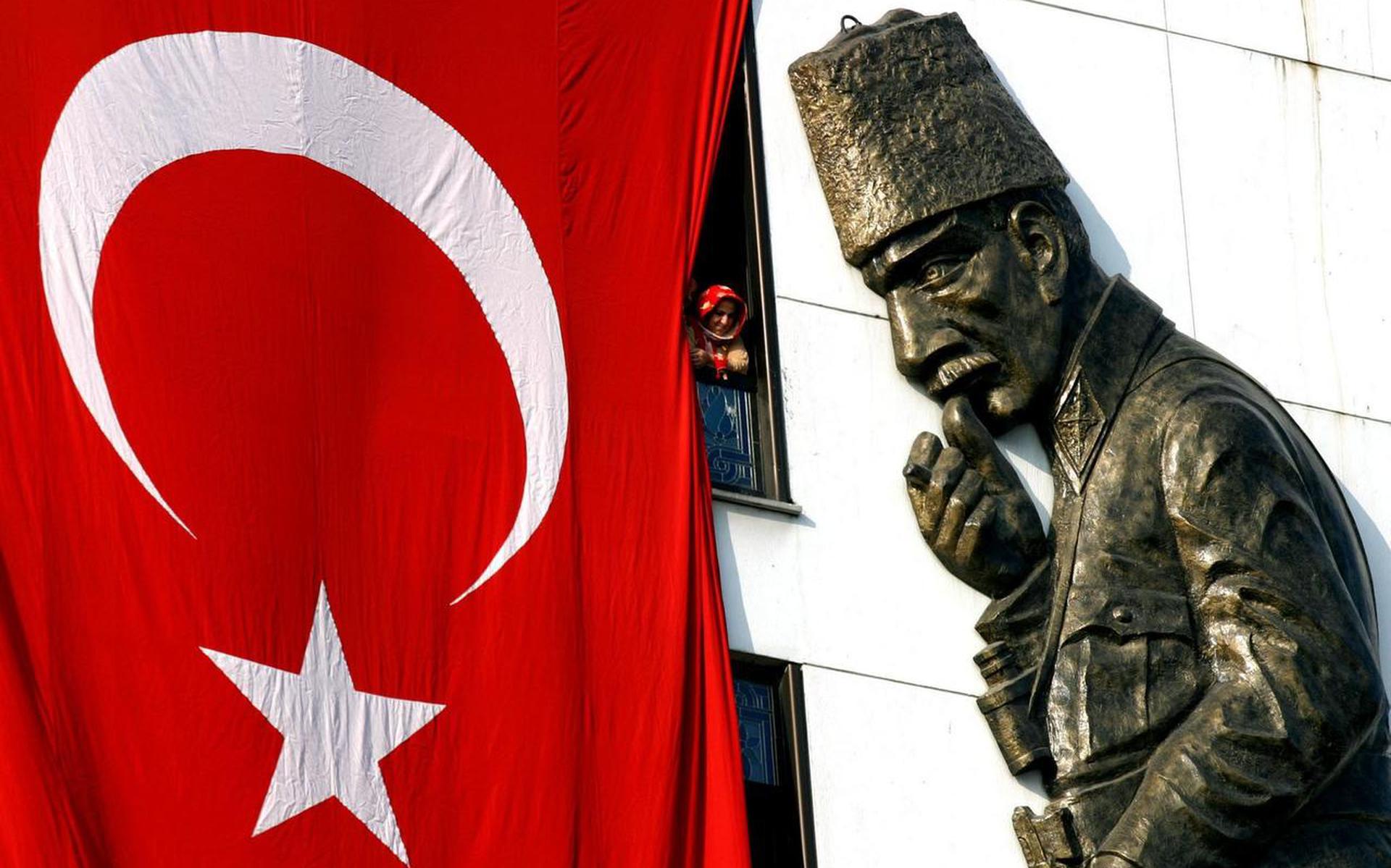 Een Turkse moslima kijkt vanachter de Turkse vlag naar het beeld van Kemal Atatürk.