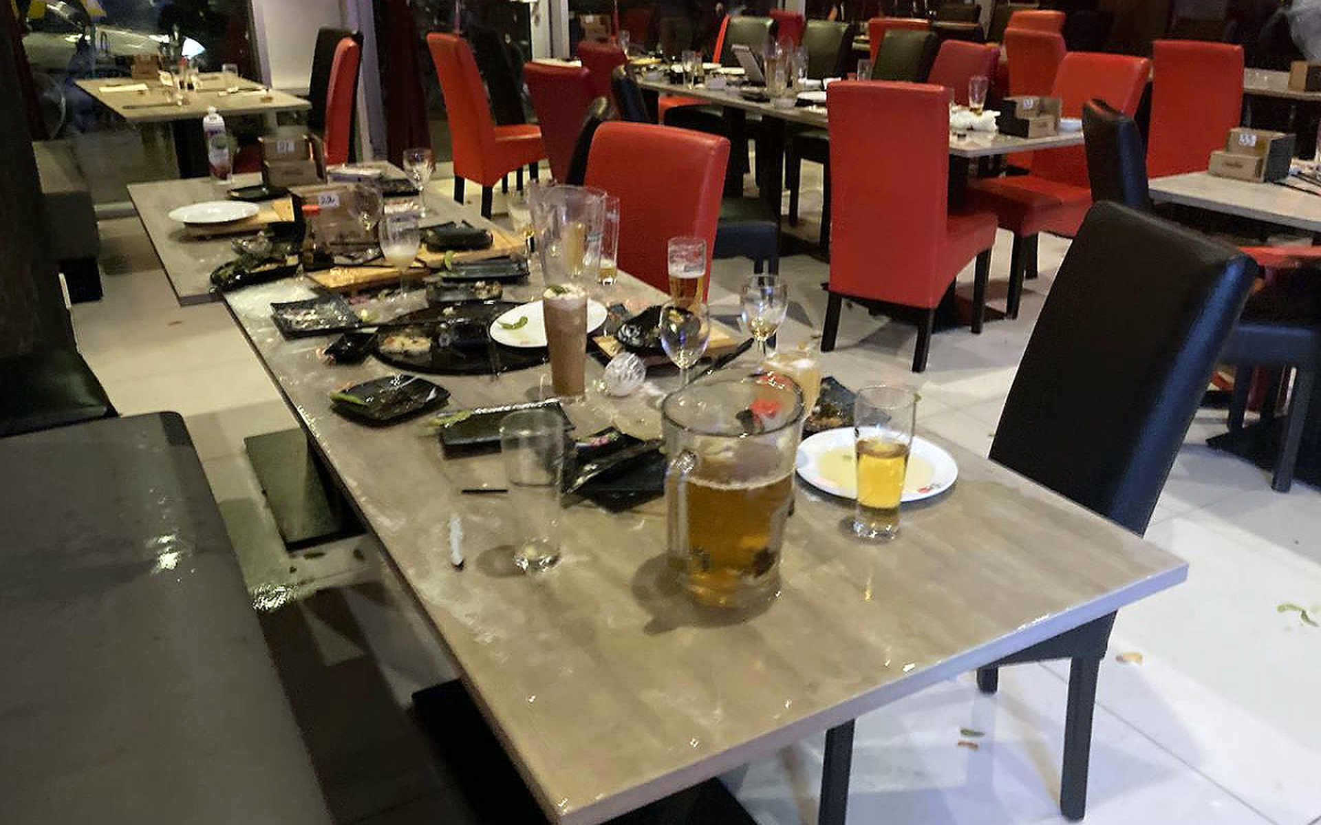 De achtergelaten chaos in het restaurant met etensresten en bier op de tafels, stoelen en de grond.