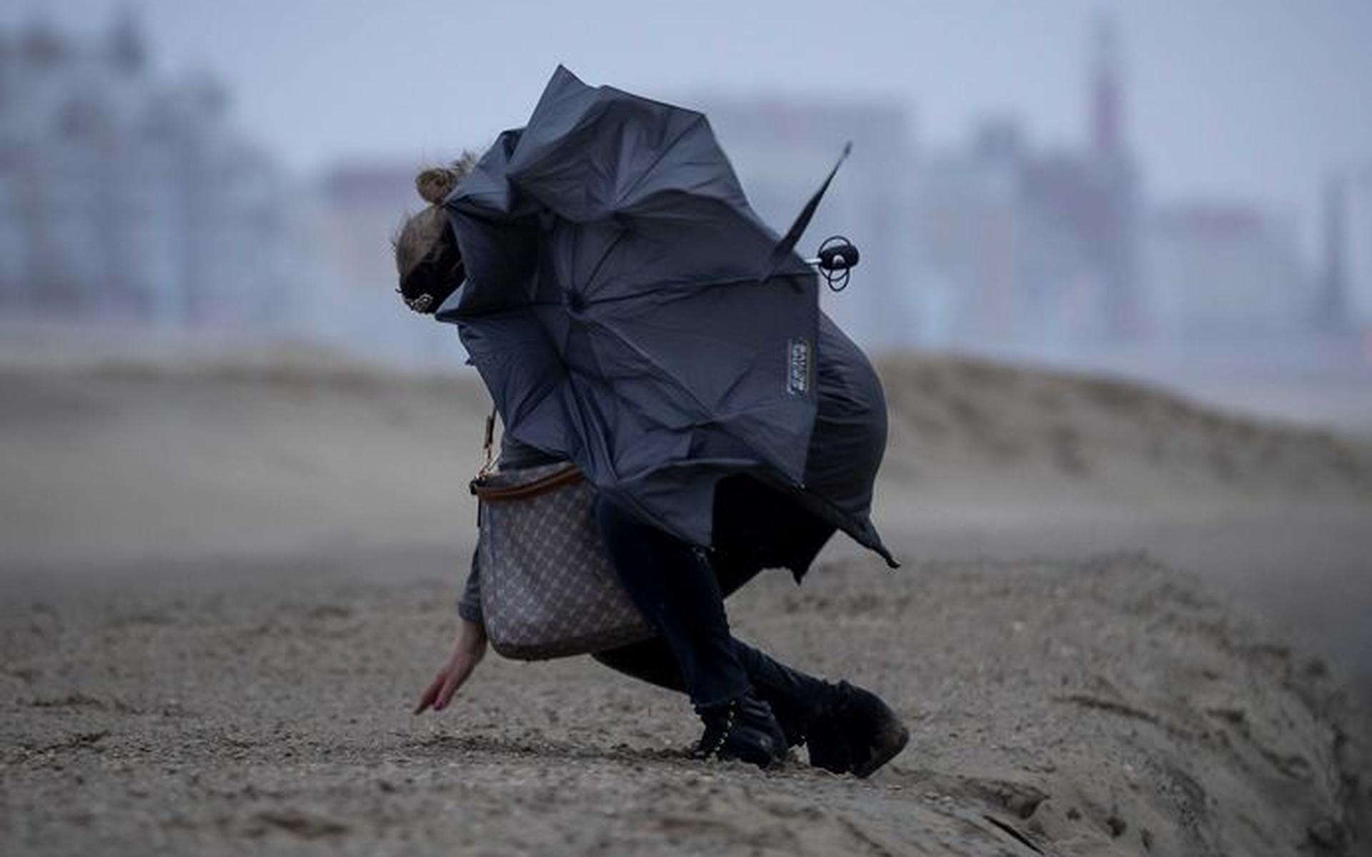 Een vrouw met een kapotte paraplu viel om door storm Ciara op het strand van Scheveningen.