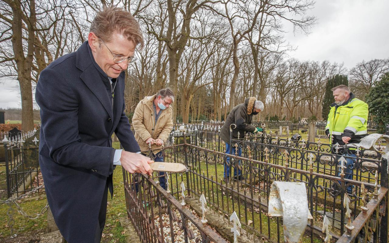 Minister Sander Dekker met roestborstel aan het werk op de begraafplaats in Veenhuizen met werkmeester Albert Eissens (gele jas) en twee tewerkgestelden. 