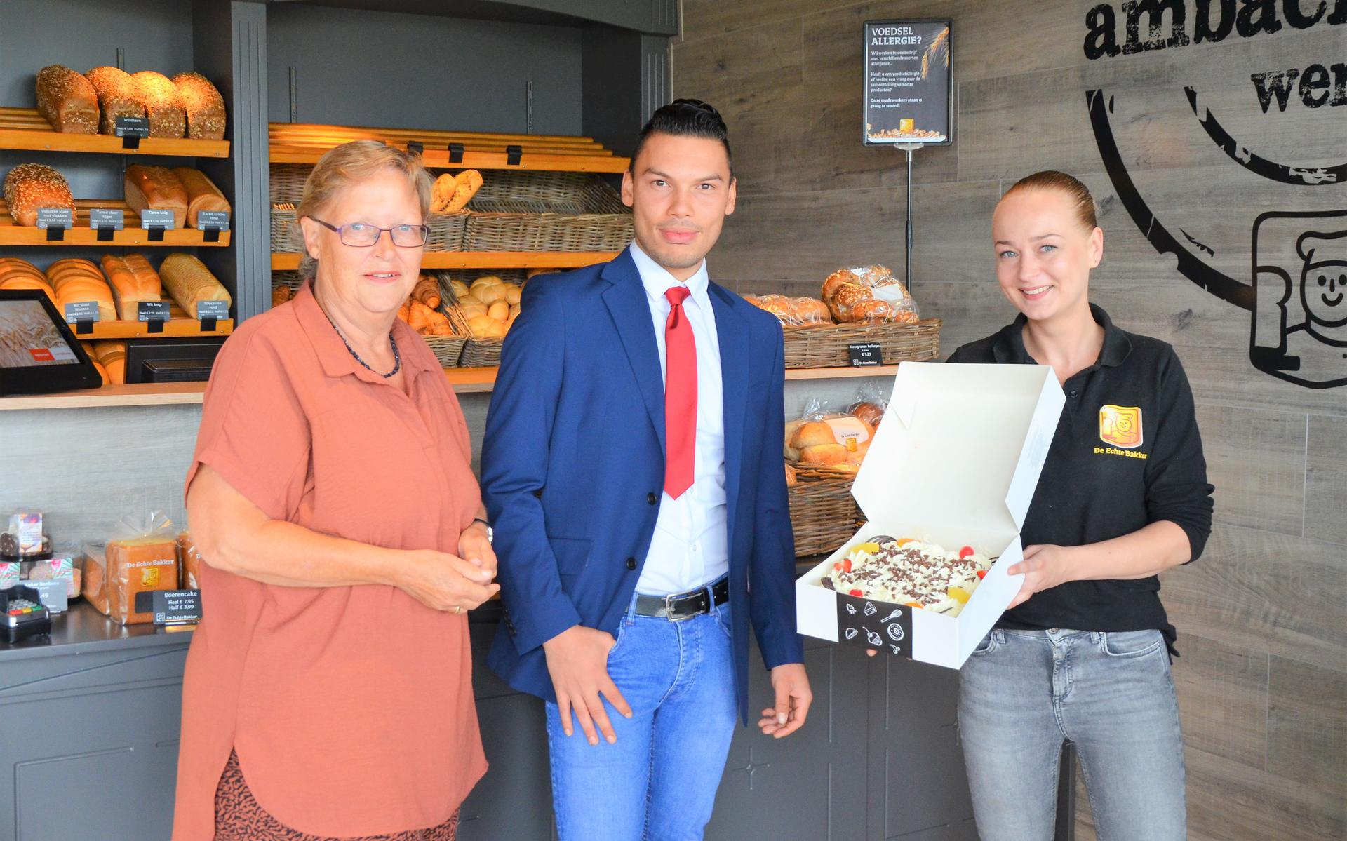 Celine Timmermans reikt de taart uit aan Nettie Bulthuis en Marcello van der Klok. 
