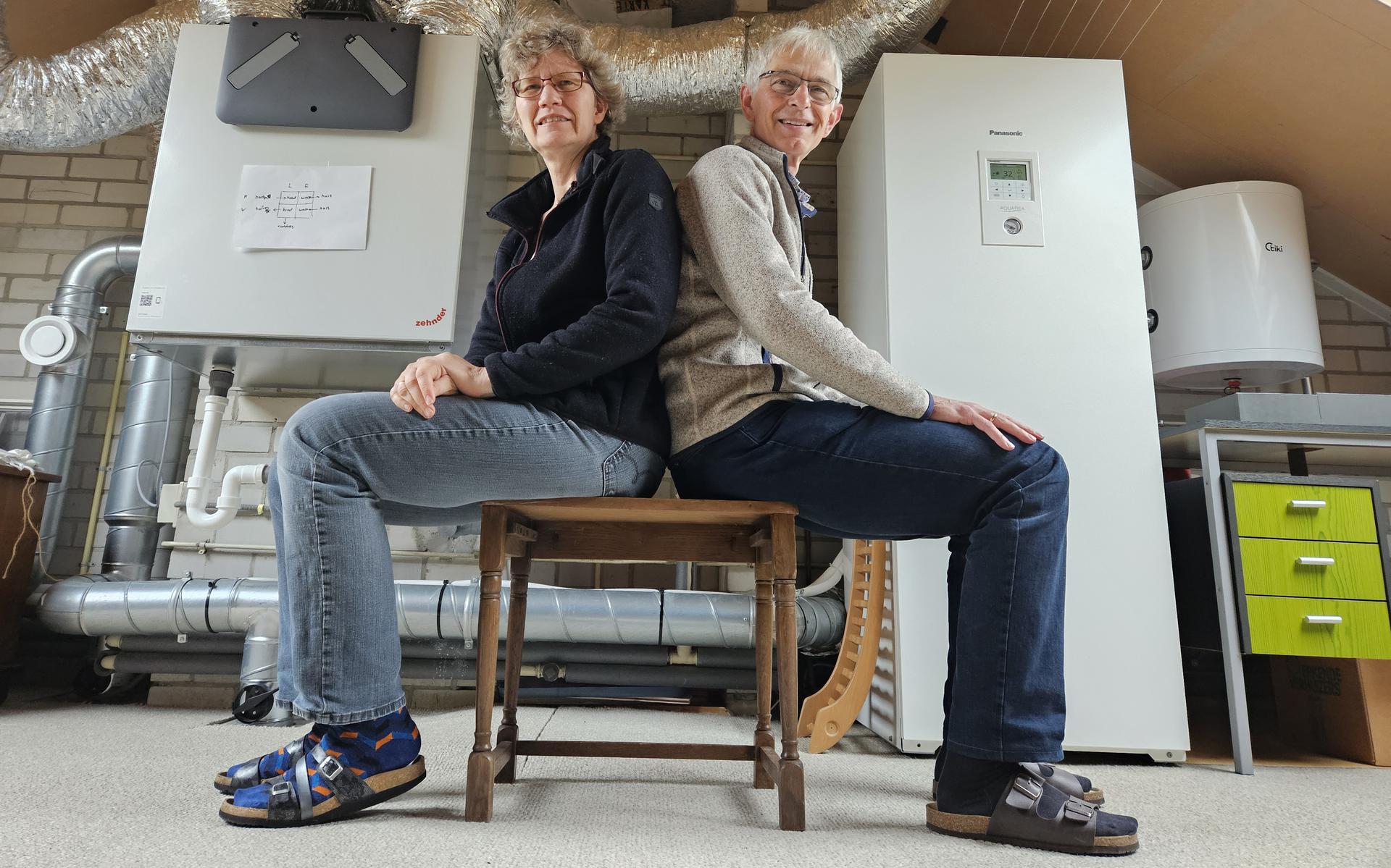 Nynke en Jaap Dijt zitten op hun zolder. Links hun balansventilatie met warmteterugwinning en rechts de warmtepomptank van 185 liter voor warm water in de keuken en douche. 