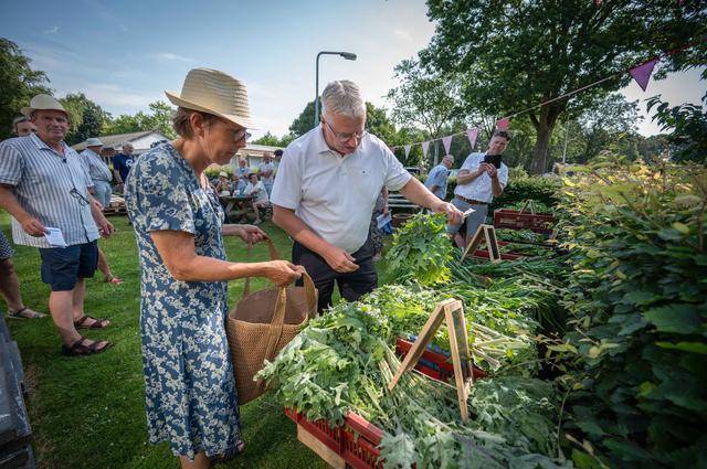 Eerste oogst uit de Kas van de Ontmoeting. Burgemeester Jan Zwiers stelt een tasje met groenten same