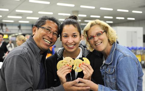 Ranomi Kromowidjojo in 2014 op Schiphol met de handen vol met medailles uit Doha tussen haar moeder Netty en vader Rudi. 