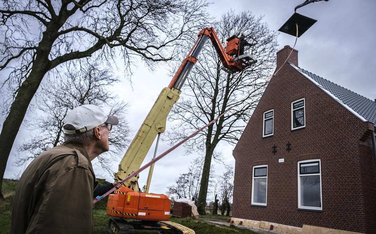 Jan Munneke kijkt hoe de nieuwe schoorsteenkap wordt geplaatst bij boerderij 't Noorn door twee hoogwerkers
