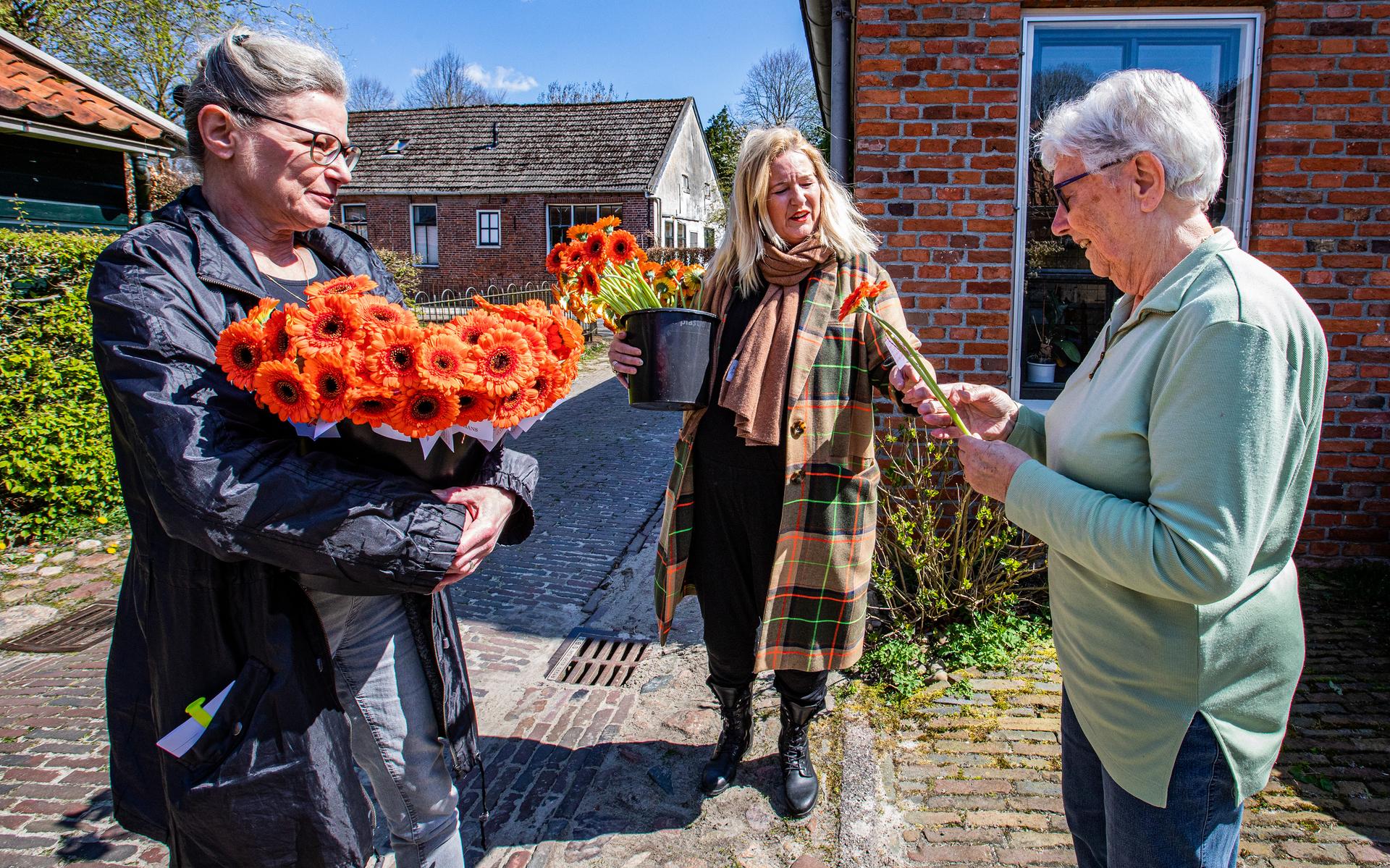 Renske Lambeck (midden) en Wilma Fonteijn (links) delen bloemen uit aan de inwoners van Oudeschans.