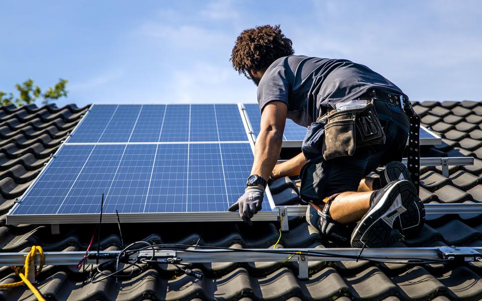 Een installateur plaatst zonnepanelen op het dak van een woonhuis. 