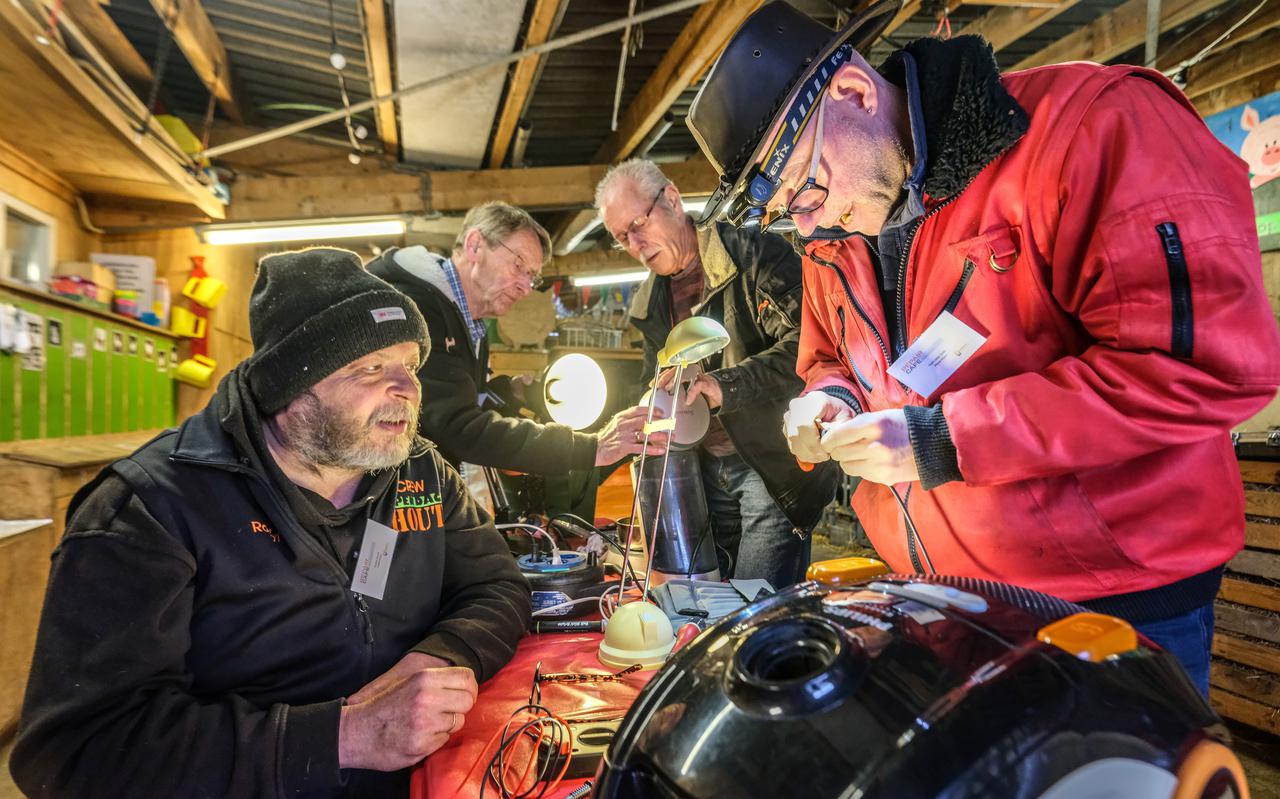 Roelof Struik (links) van het Repair Café kijkt toe hoe Gert-Jan Span een stofzuiger repareert. Op de achtergrond de vrijwilligers Joop Luurtsema (links) en Richard Kok.