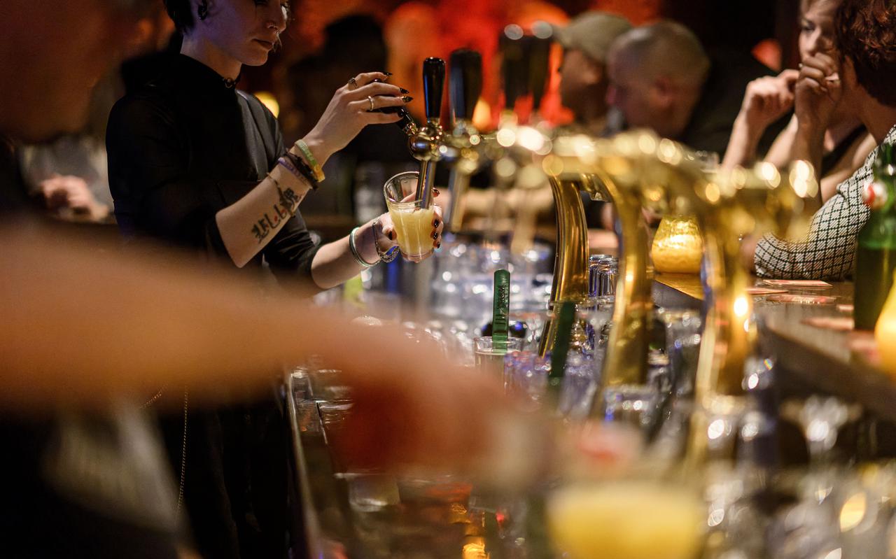 Een barkeeper tapt op zaterdagavond bier in een drukbezocht café.