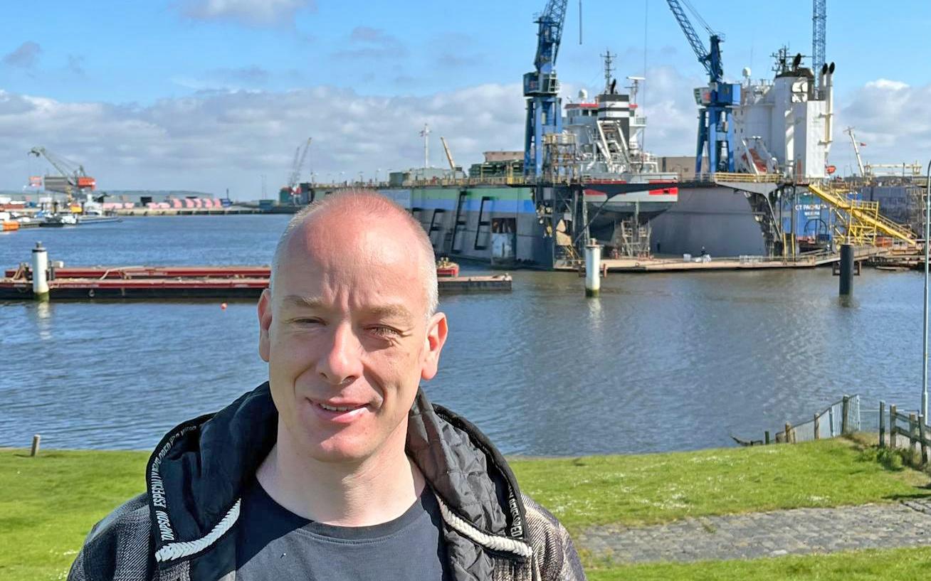 Mark Giesolf op de dijk voor het reparatiedok van Niestern Sander, waarin tijdens de Pinkstertrail een groot schip ter reparatie ligt.