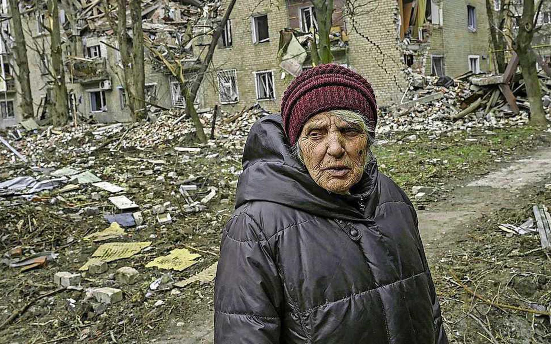 Een vrouw staat voor een verwoest flatgebouw in Avdiivka. Veel oudere inwoners van de stad weigeren hun woonplaats te verlaten.