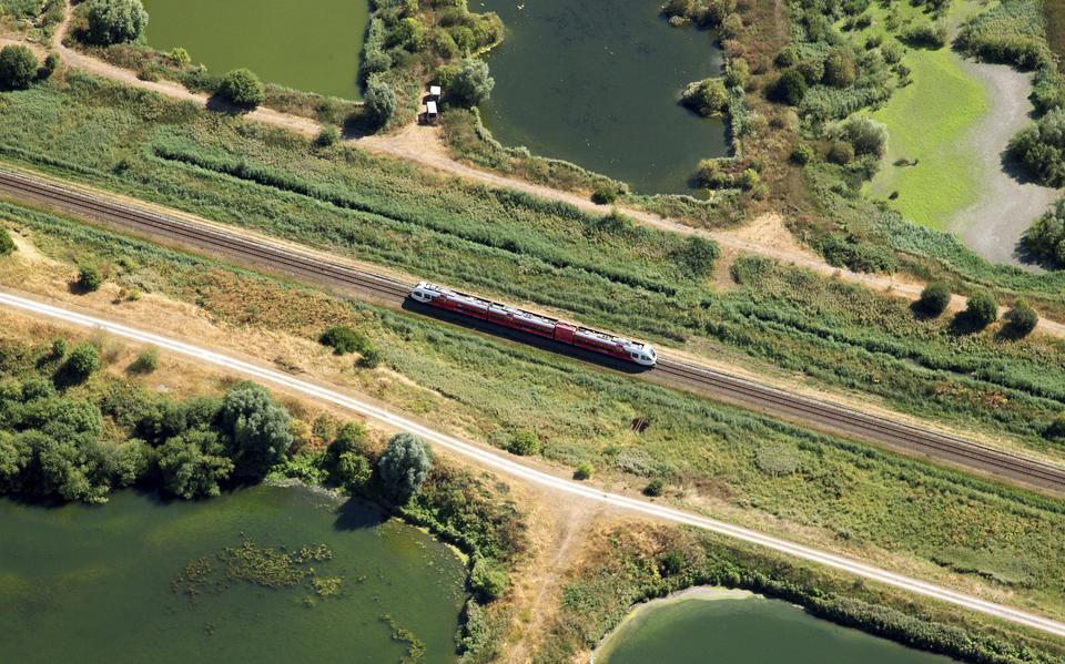 Een rode Arriva-trein tussen de vloeivelden van de voormalige suikerfabriek in Groningen. Ongeveer op deze plek is het nieuwe station Suikerzijde gepland. De gelijknamige woonwijk (8000 huizen) komt aan weerszijden van het spoor te liggen.