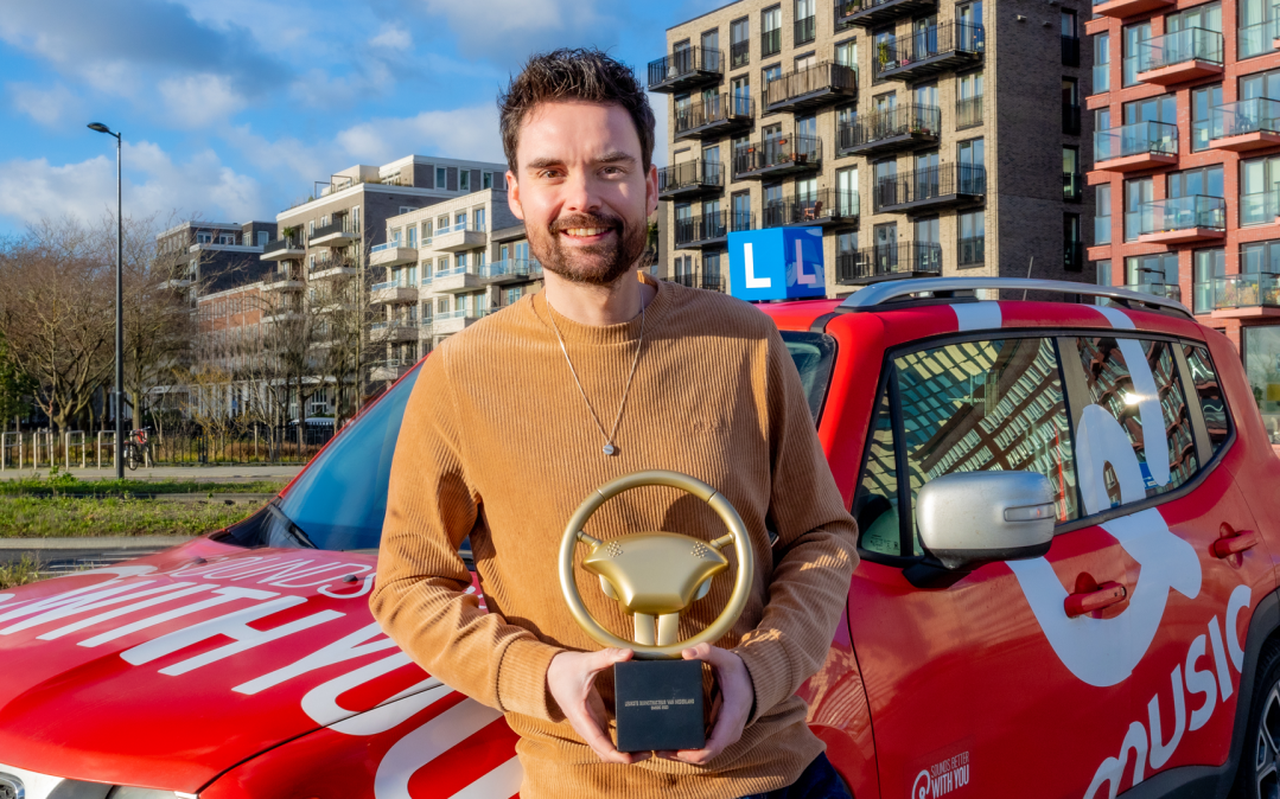 Qmusic radio-dj Domien Verschuuren met in zijn handen het gouden stuur voor de Leukste rijinstructeur van Nederland. FOTO: Qmusic