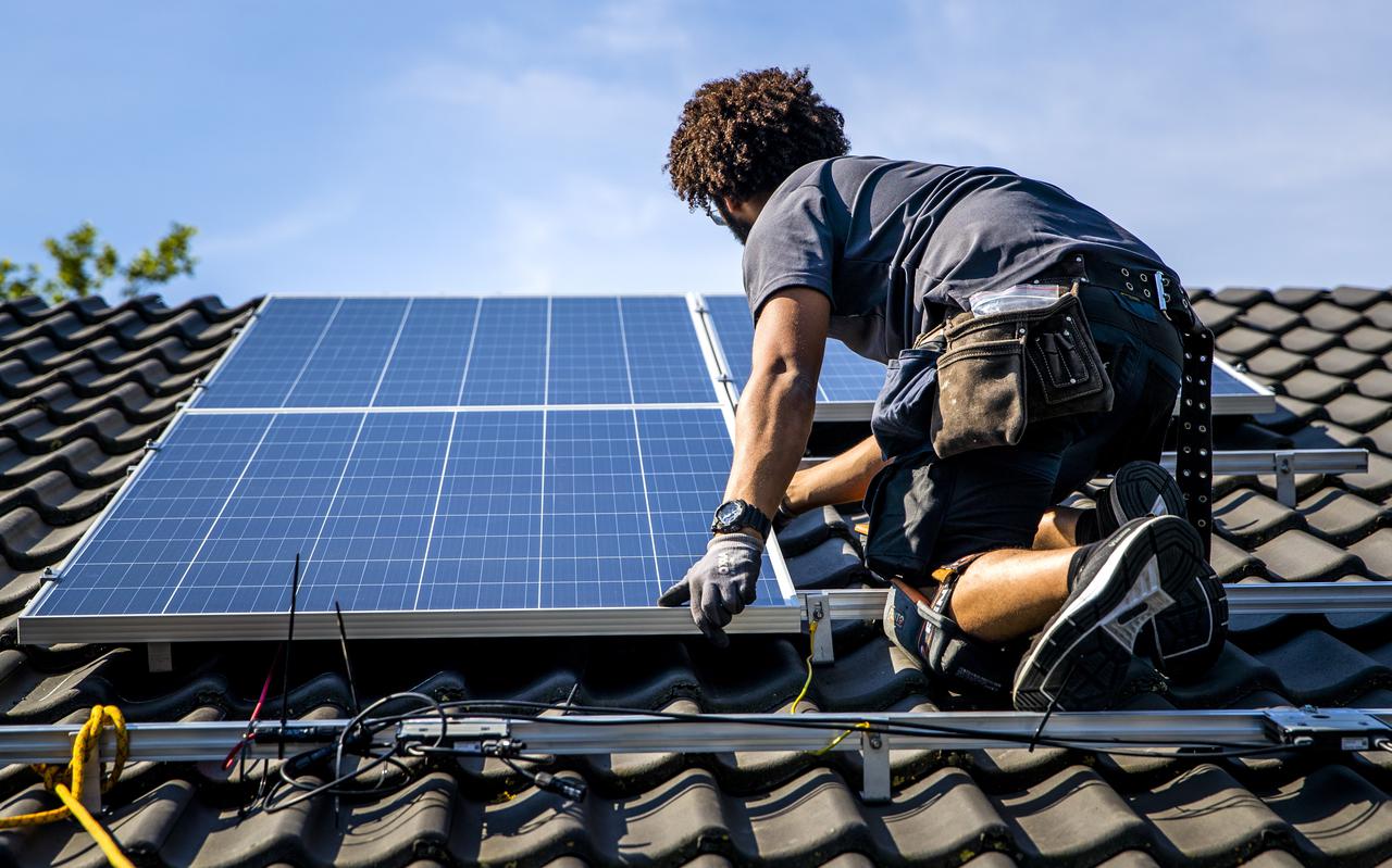 Een installateur plaatst zonnepanelen op het dak van een woonhuis.
