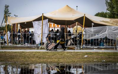 Zonder tentjes schuilen asielzoekers onder de luifel voor het asielcentrum in Ter Apel voor de regen van woensdag. Voor de nacht hoopt het COA iedereen wel onder dak te hebben.