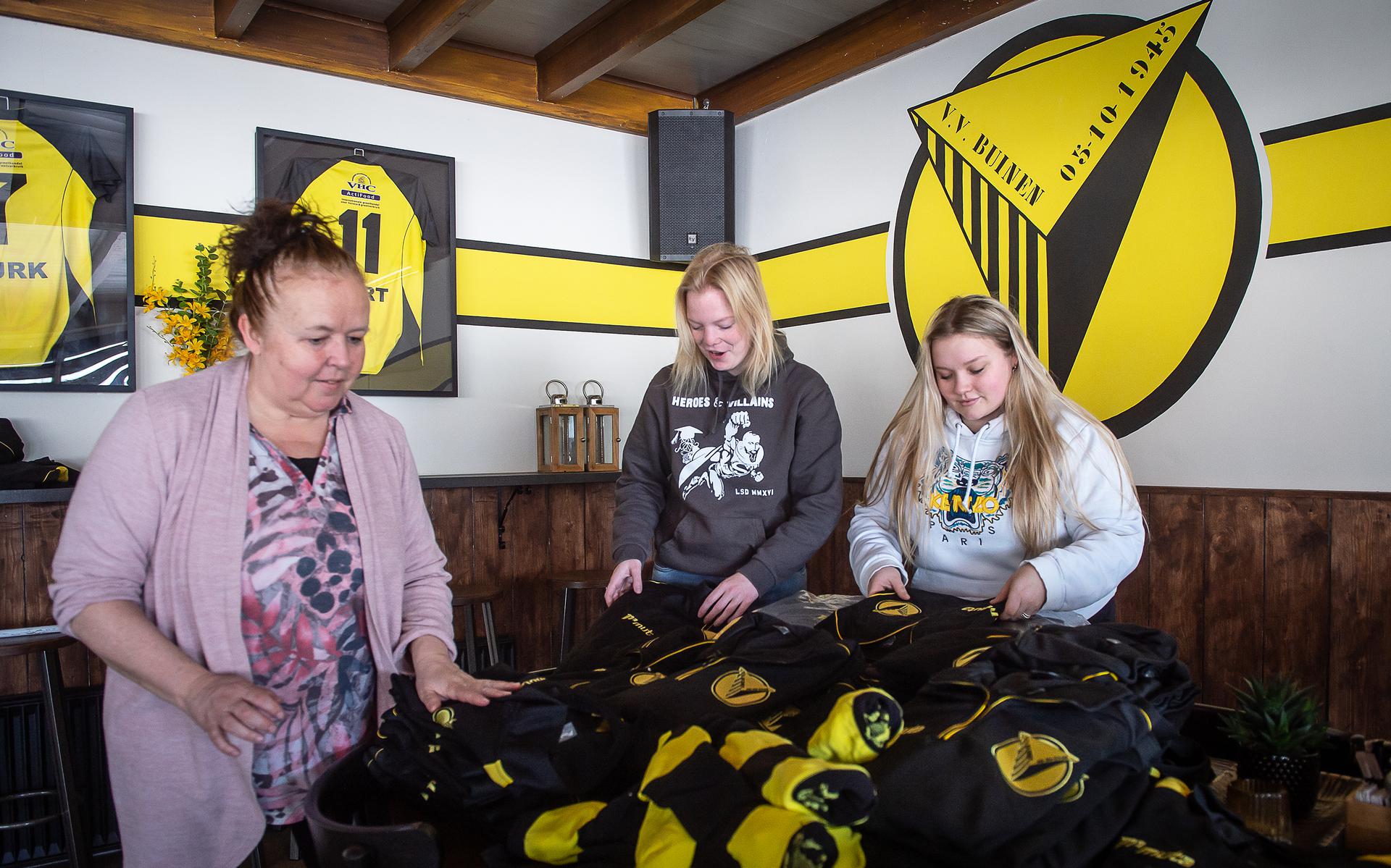 Anja Beerman, Lisa Huizing en Alisa Beerman (v.l.n.r.) sorteren in de kantine van VV Buinen voetbalkleding.