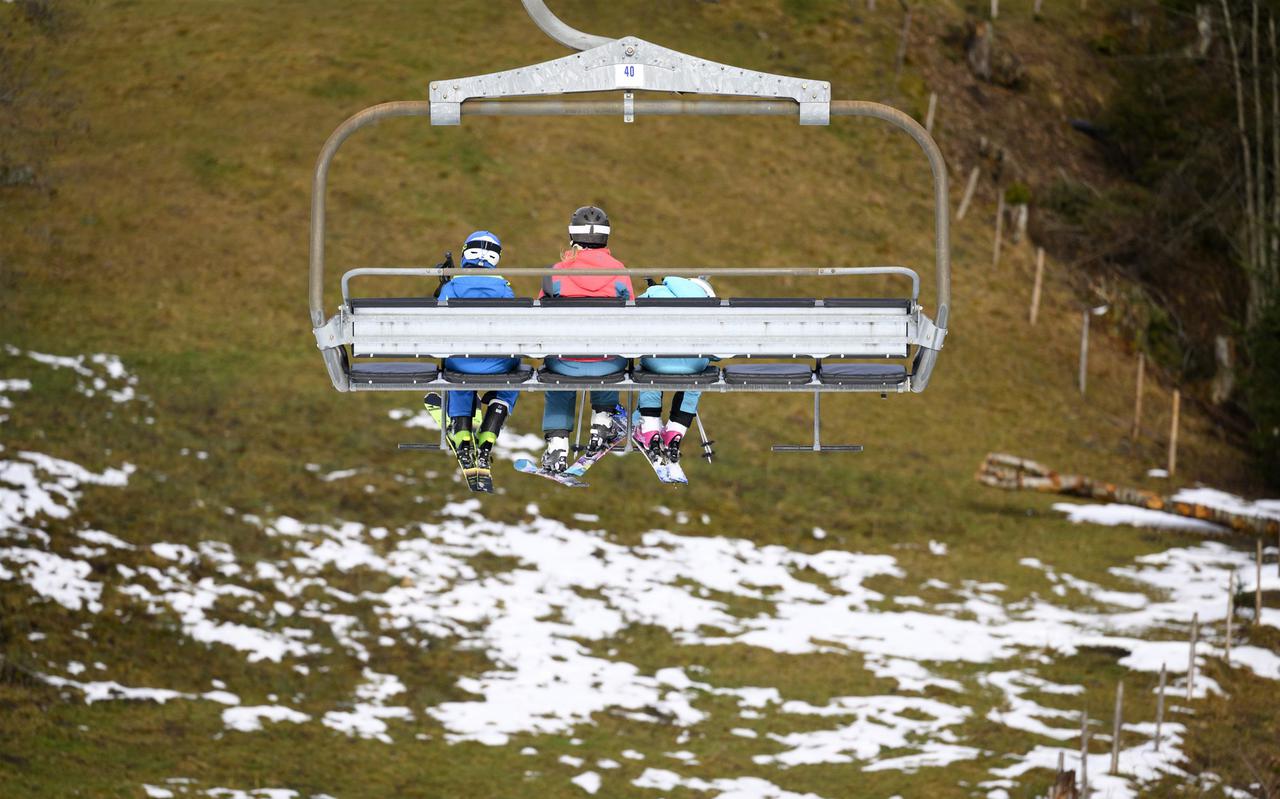 Skiërs in een stoeltjeslift boven een sneeuwloos veld, Villars-sur-Ollon, Zwitserland, 31 december 2022.