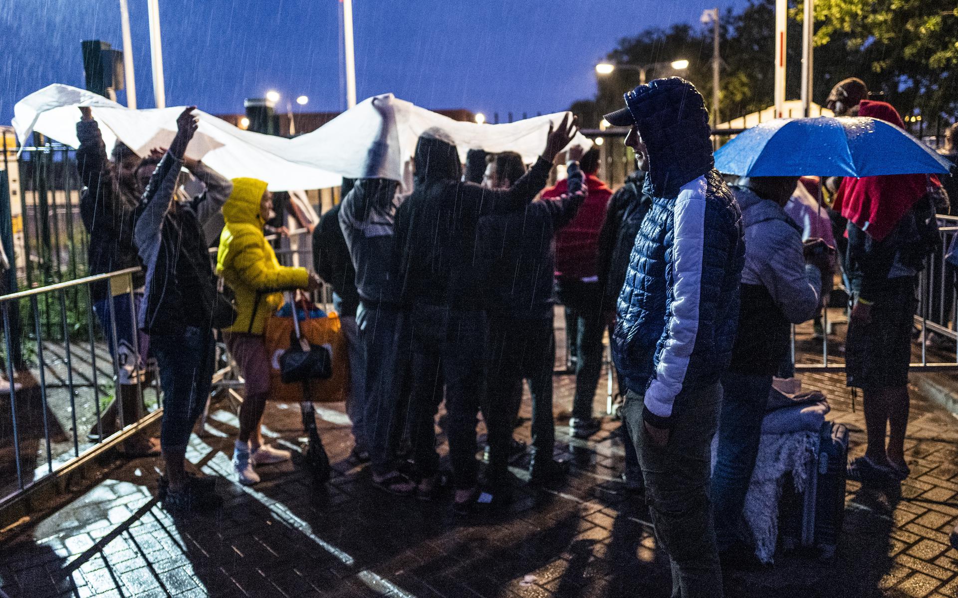 Asielzoekers zoeken beschutting tegen de regen voor de poort bij het overvolle aanmeldcentrum in Ter Apel. Dit was het beeld in 2022.