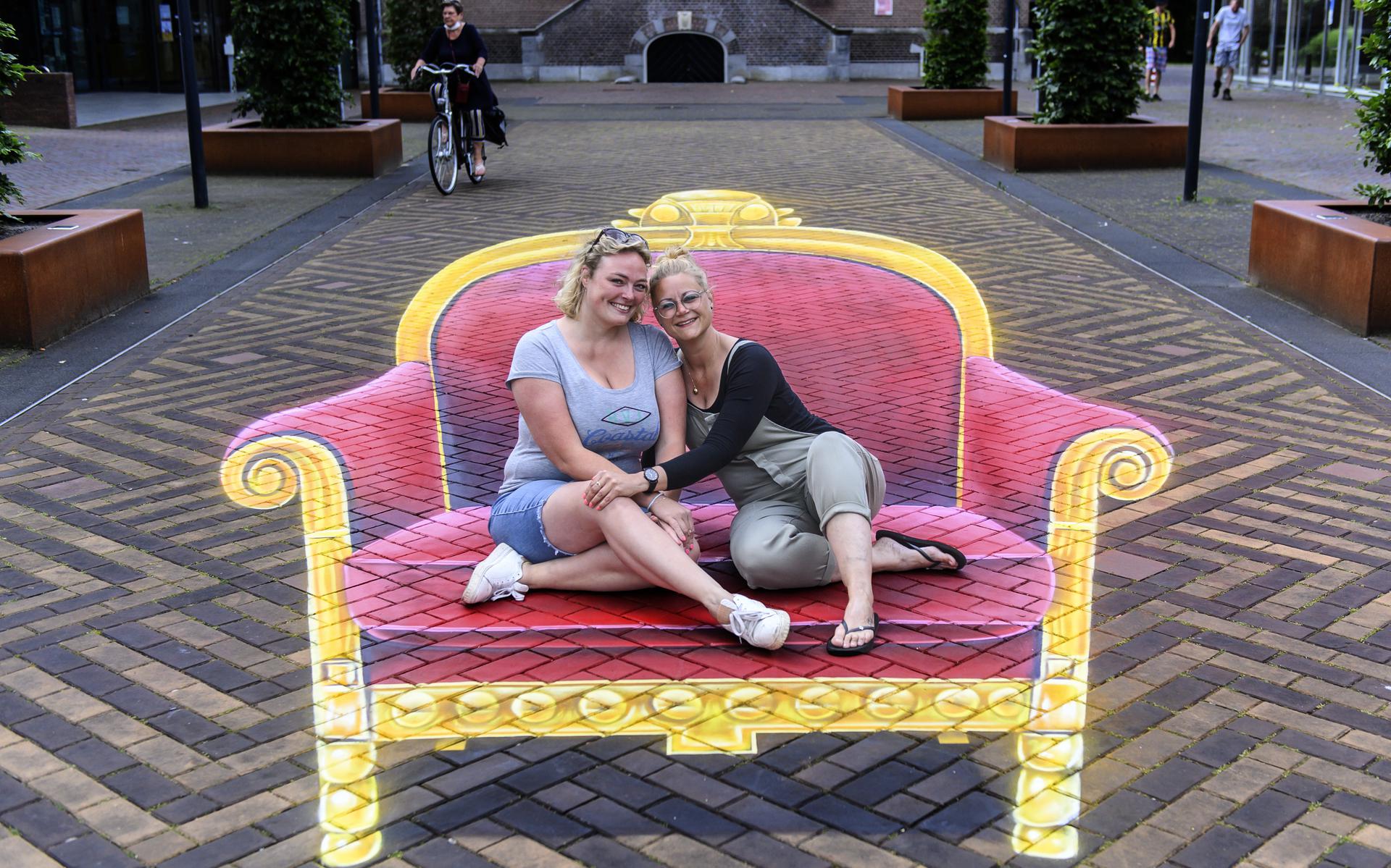 Evelyn van Buizen (links) en Miranda Dijkstra lijken op een kleurige stoel op het Raadhuisplein in Veendam te zitten. Optisch bedrog. In werkelijkheid zitten ze op de straat.