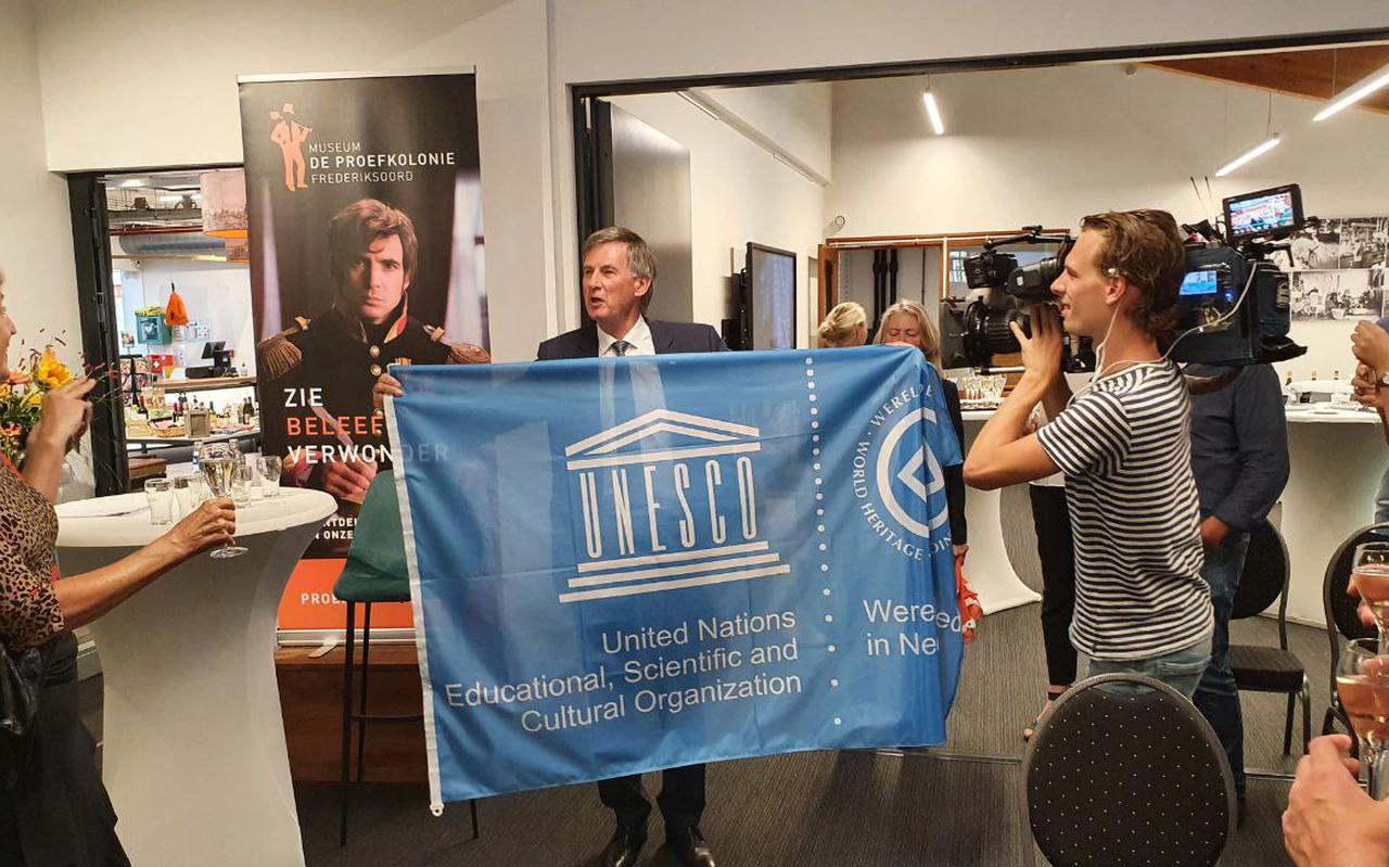 Gedeputeerde Cees Bijl laat na de toekenning van de werelderfgoedstatus trots de Unesco-vlag zien aan de zaal in Museum de Proefkolonie in Frederiksoord.  Foto: DvhN