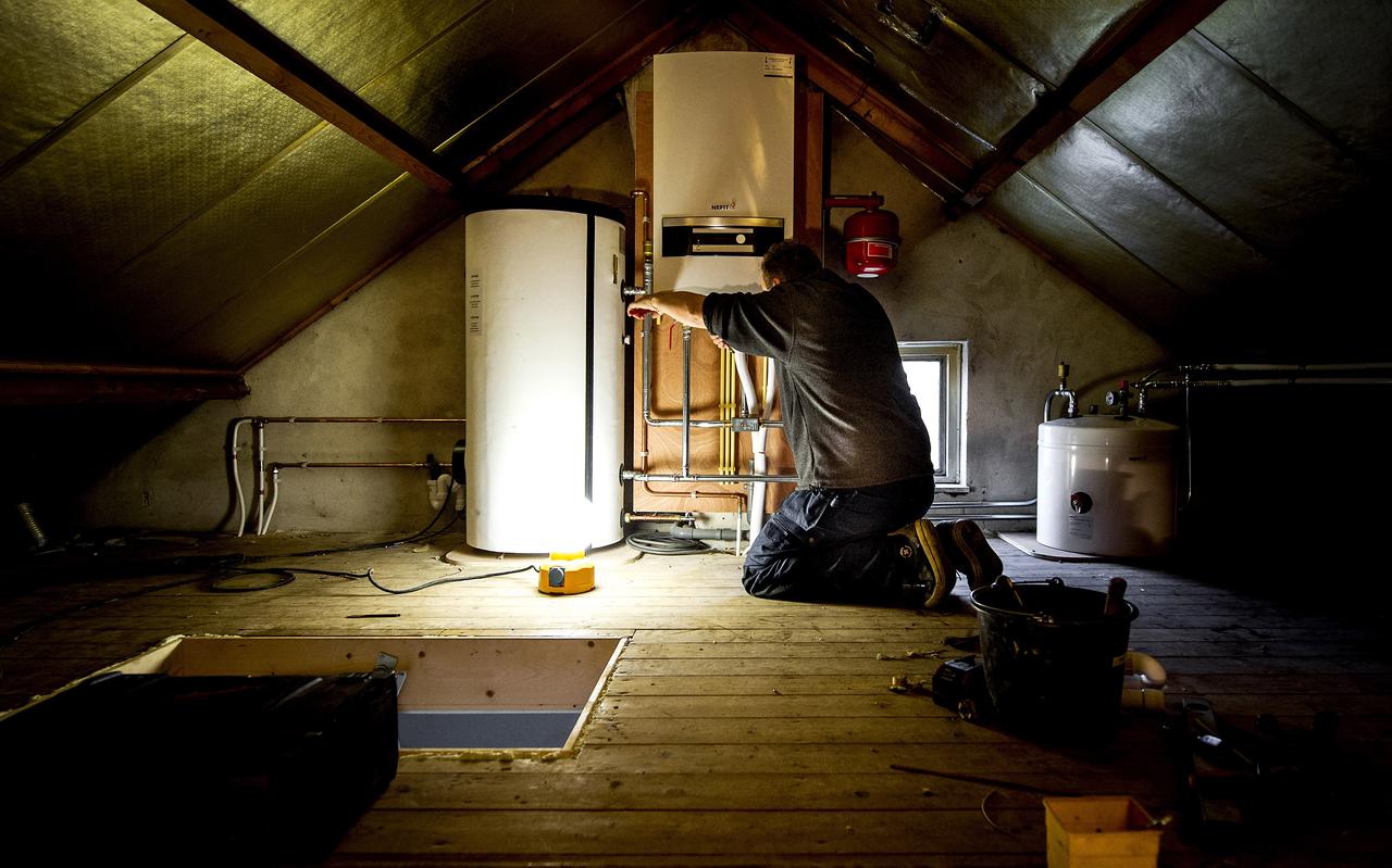 Een installateur installeert een hybride warmtepomp bij een cv-ketel in een woning uit de jaren zestig. De gasloze cv-ketel die in het Noorden wordt geproduceerd, kan het water anderhalf keer warmer maken dan een reguliere warmtepomp.