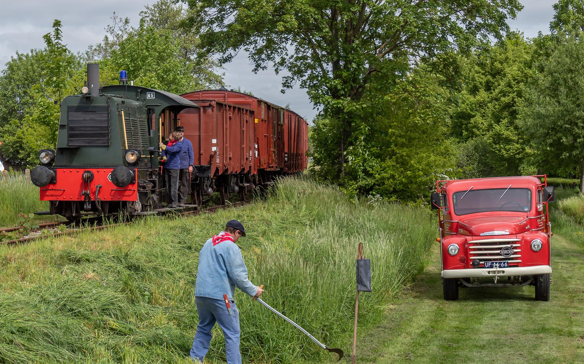De goederentrein voor Nieuw-Buinen heeft station Stadskanaal achtergelaten. De boerenknecht staat rustig het gras te maaien.
