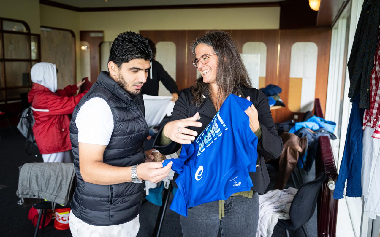 Vrijwilliger Willemijn Kemp (r) uit Haren hoopt vluchteling Mohammed Halima tijdens een kledingbeurs blij te maken met een van de vele gedoneerde sportshirts.