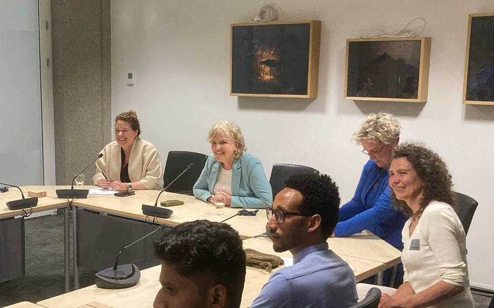Minister Pia Dijkstra van Volksgezondheid (midden achter) praat in een vergaderzaal in de Tweede Kamer met een groep asielmigranten die in de zorg werken. 