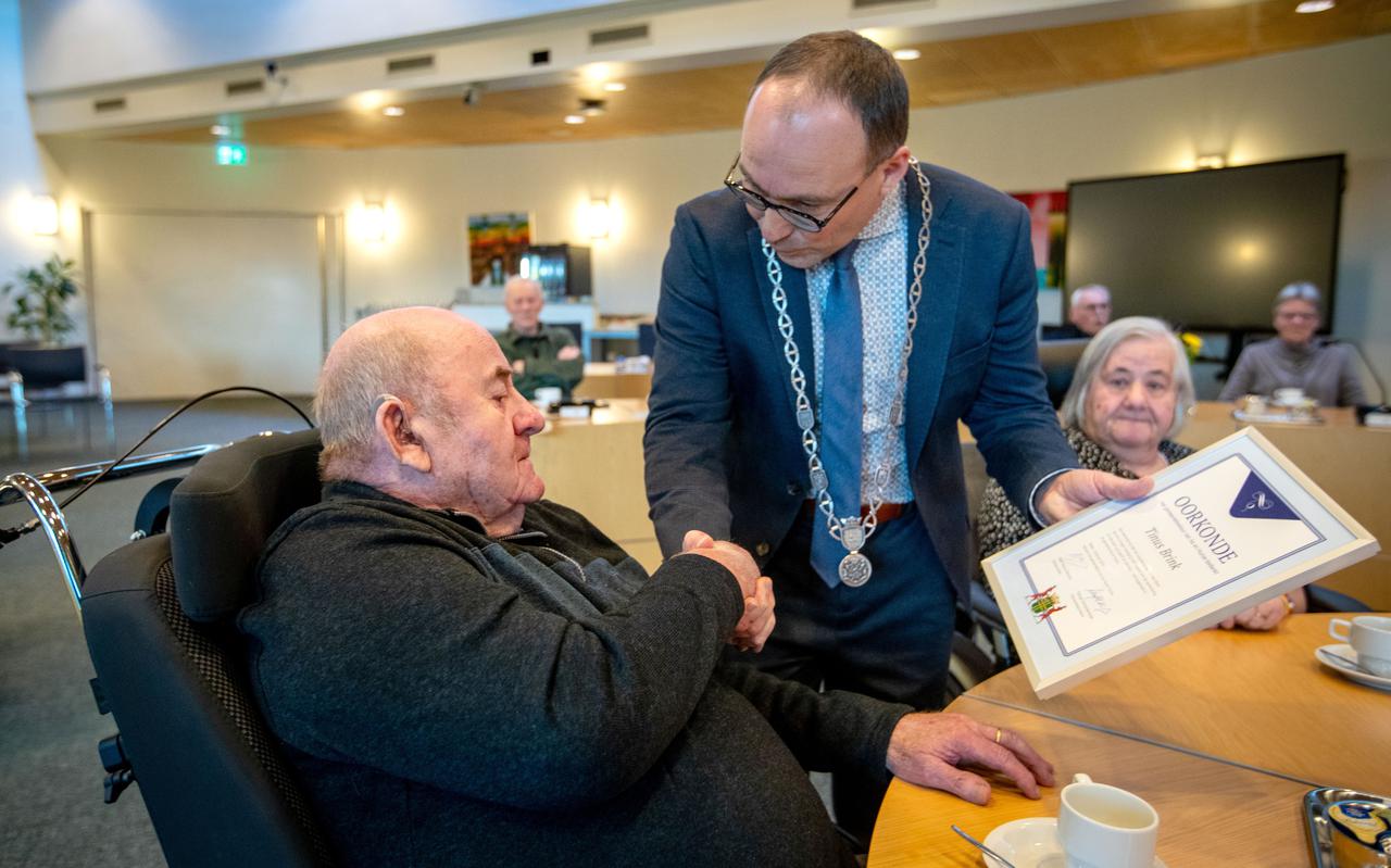 Rooie Tinus ontvangt van burgemeester Hiemstra een oorkonde voor zijn werk in de gemeente Aa en Hunze. Brink heeft zo'n 50 jaar oud papier en ijzerwaren opgehaald in de gemeente.