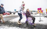 Een GGD-medewerker helpt een vrouw in een rolstoel door de sneeuw bij de coronalocatie in Assen, februari 2021.
