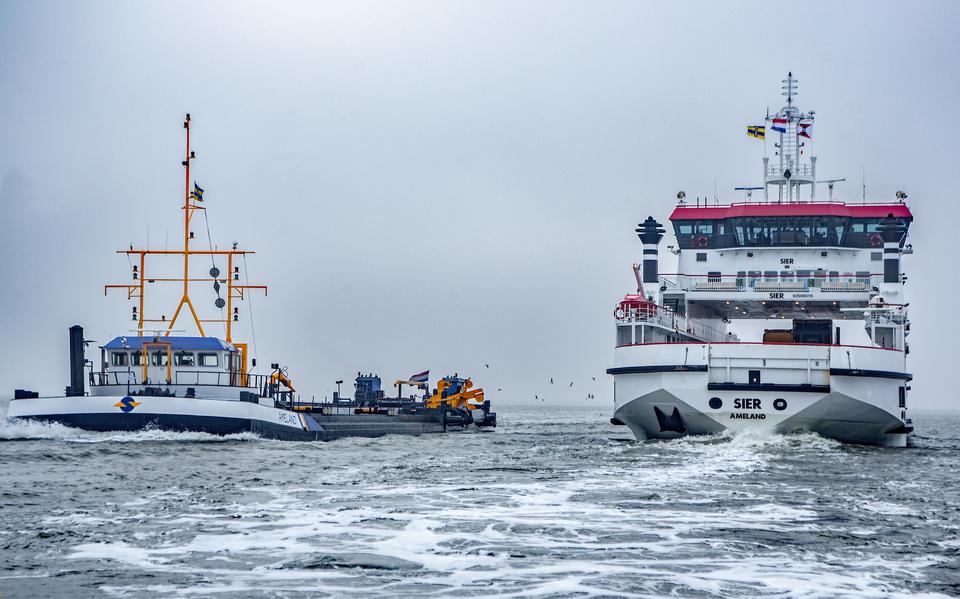 Veerboot De Sier haalt op de hoofdvaargeul naar Ameland een baggerschip van Rijkswaterstaat in. 